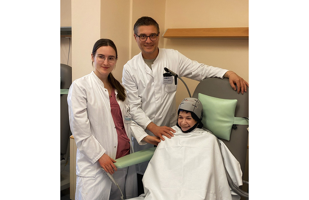 Assistenzärztin Veronika Radzikhovskaya, Klinikdirektor Prof. Dr. Atanas Ignatov und Chemofachschwester Annette Ahlemann zeigen die Anwendung der Kopfhautkühlung, demonstriert von Annette Ahlemann in der Rolle der Patientin.