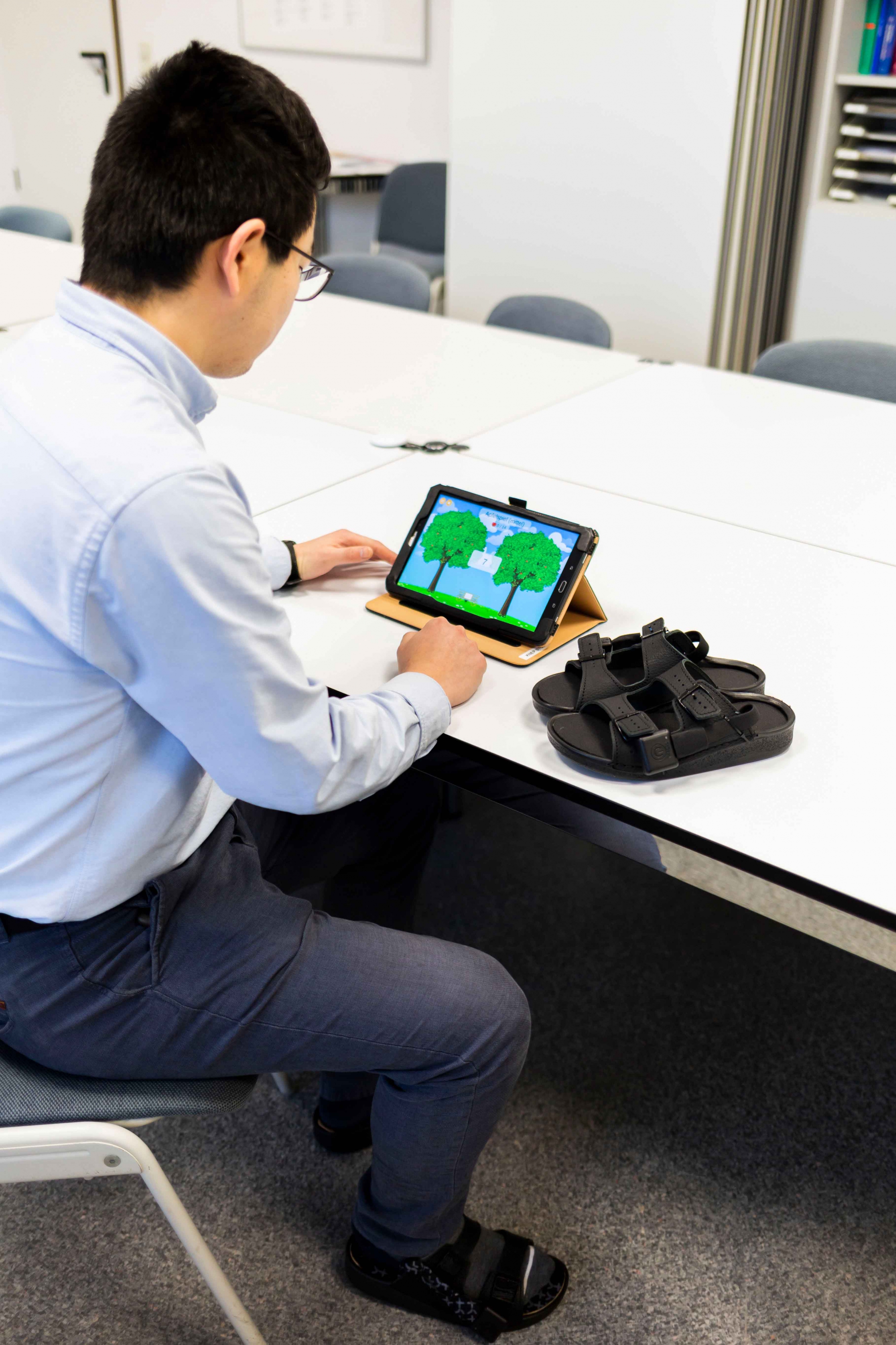 Wissenschaftlicher Mitarbeiter Antao Ming demonstriert die Funktionsweise der Sohle in Verbindung mit dem Spiel auf einem Tablet._Fotografin Sarah KossmannUMMD